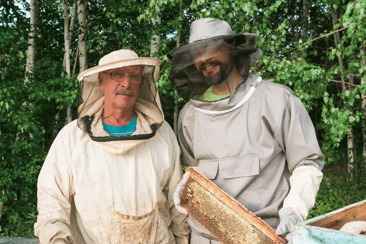 Farmer and Beekeeper Wearing Bee Suits Working with Honeycomb in Apiary