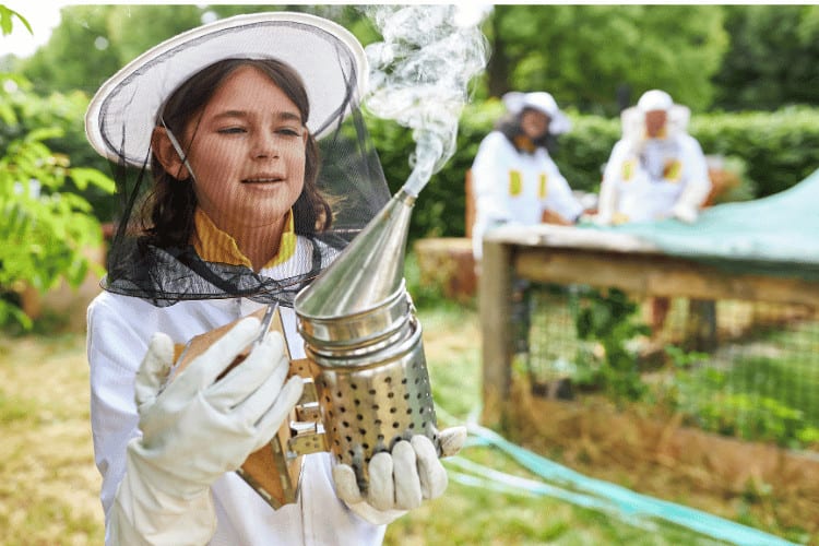 Girl as Beekeeper with Bee Smoker in Front of Bee Hives