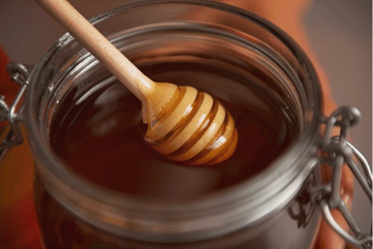 Honey dipper in glass honey jar. Closeup